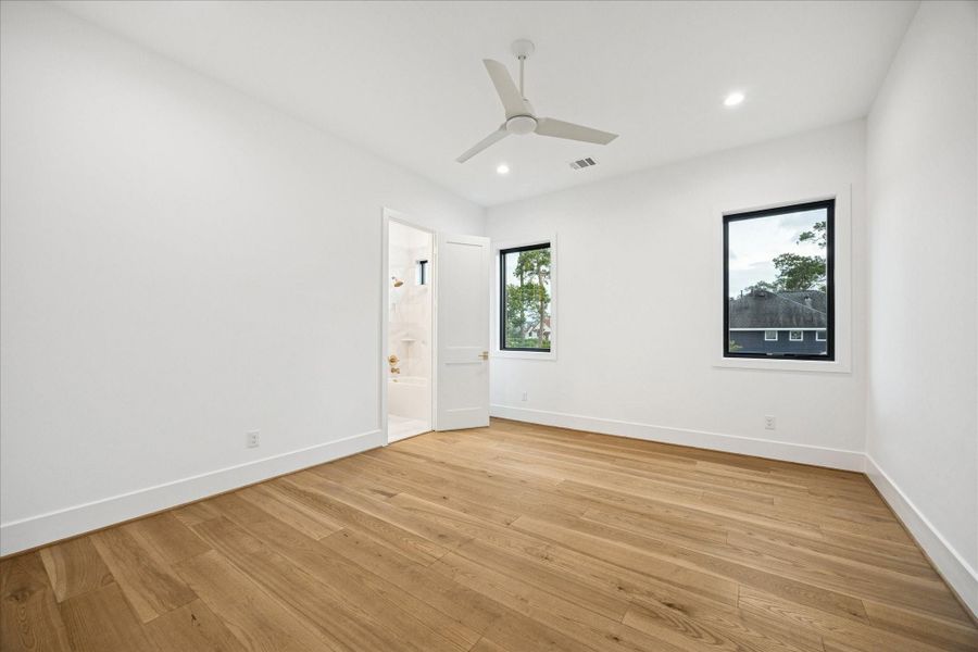 A calm, neutral palette and large windows define this secondary bedroom, complete with its own en-suite bath for a streamlined, functional layout.