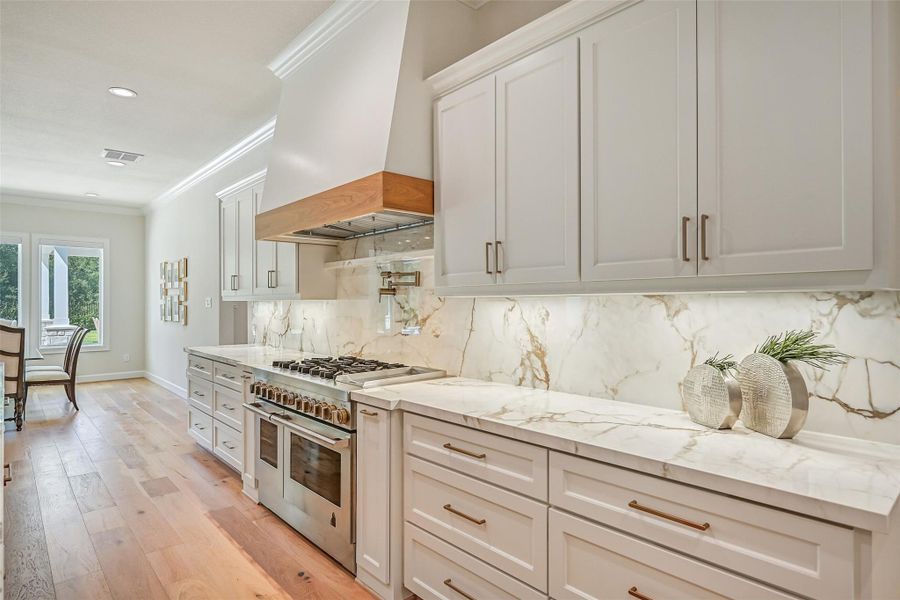 Calacatta Macchia Vecchia porcelain extends from the countertops up the full-height backsplash for a dramatic, seamless finish behind the professional-style gas range, accented by a pot filler, custom vent hood & under-cabinet lighting.