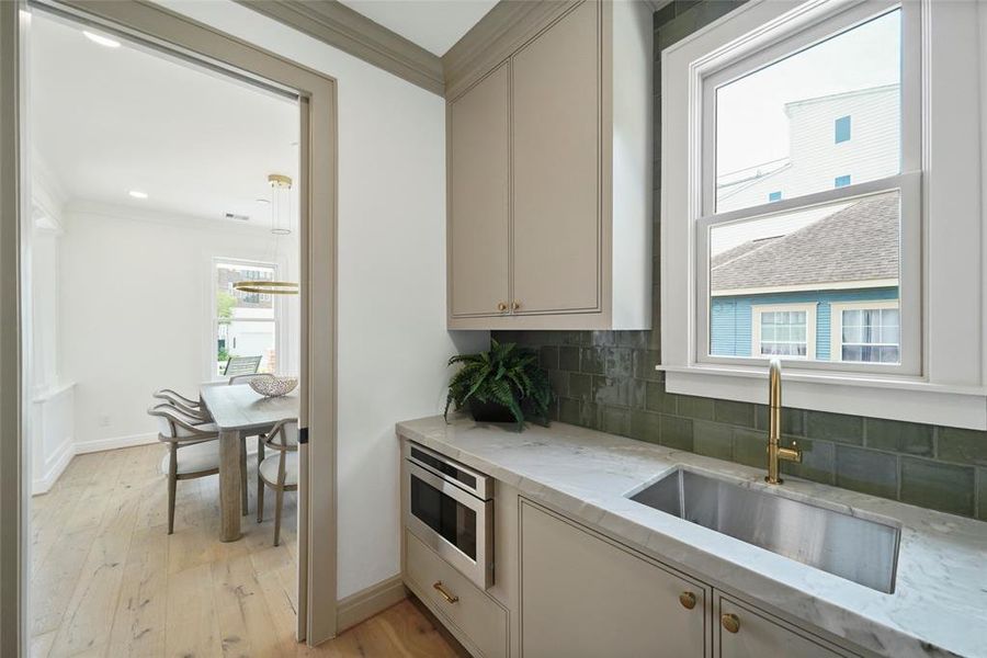 Elegant butler's pantry featuring a sink and green subway tiles, bathed in natural light from a large window with a pleasant view.