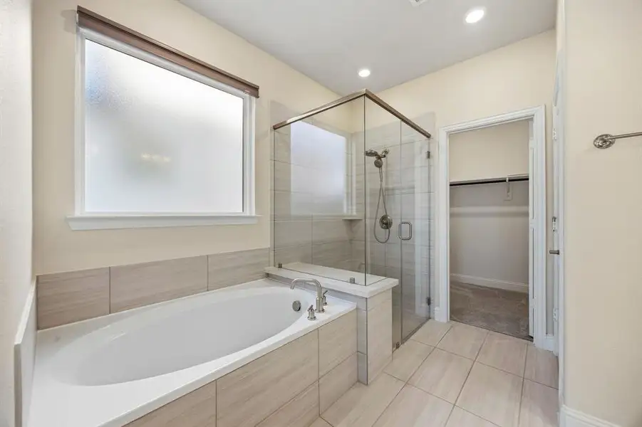 Bathroom featuring light tile patterned flooring, a bath, a shower stall, and a walk in closet
