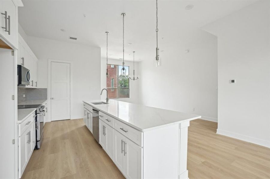 Kitchen with appliances with stainless steel finishes, a sink, light wood finished floors, and white cabinetry