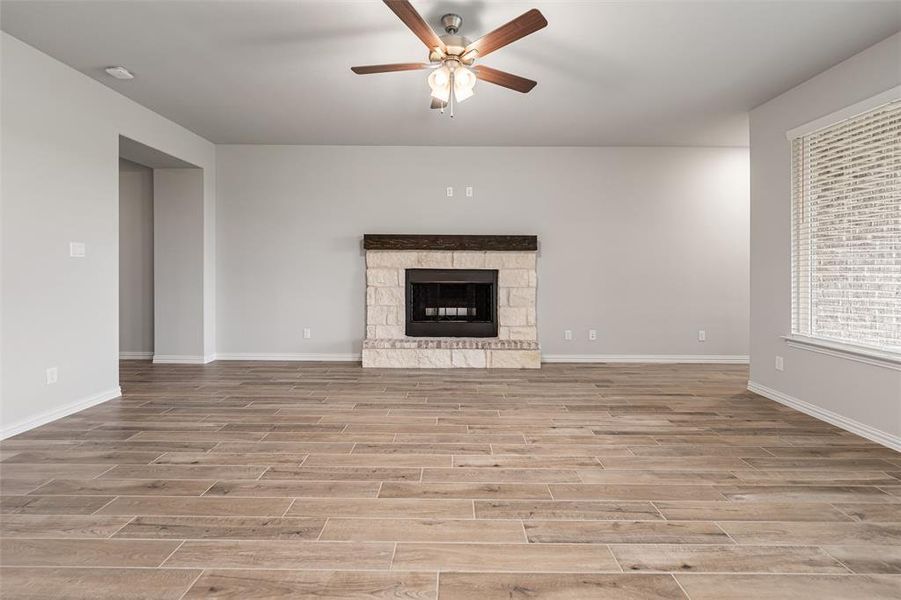 Unfurnished living room featuring a stone fireplace, light wood-type flooring, and ceiling fan Unfurnished living room featuring a stone fireplace, light wood-type flooring, and ceiling fan