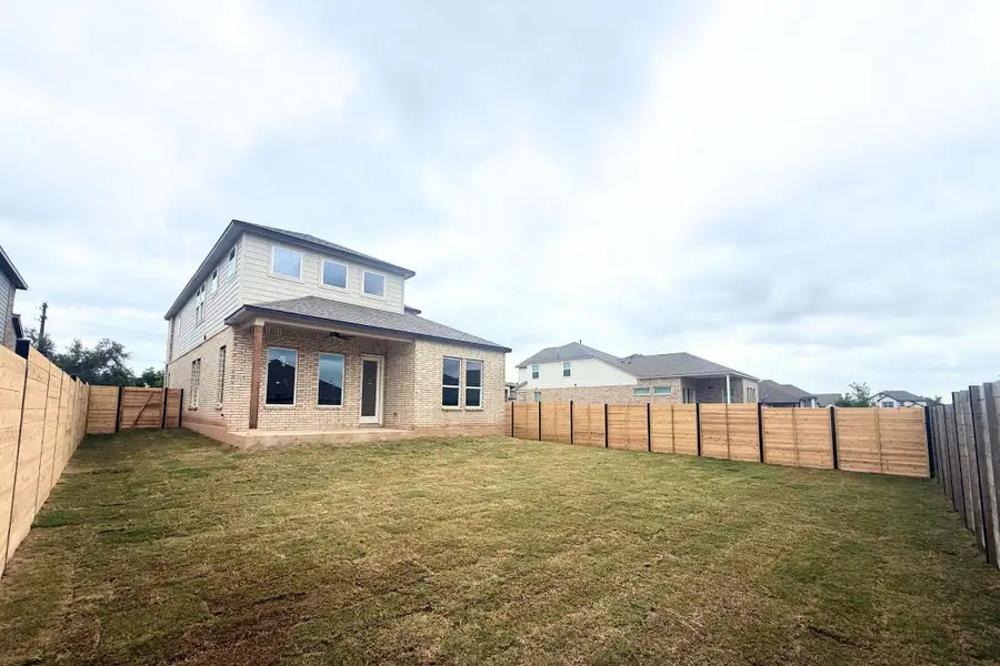 Expansive backyard featuring freshly laid sod, a newly installed horizontal plank fence, and a two-story residence with a brick and siding exterior Expansive backyard featuring freshly laid sod, a newly installed horizontal plank fence, and a two-story residence with a brick and siding exterior
