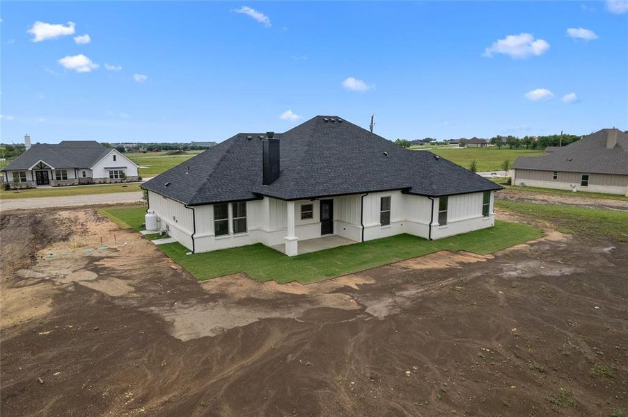 Rear view of property with a shingled roof, a patio area, driveway, and a lawn