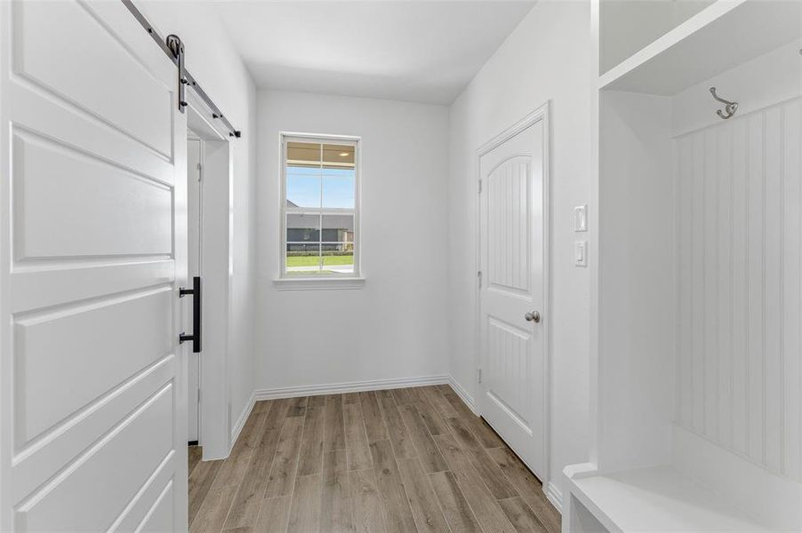 Entryway featuring wood-finish flooring, a white paneled barn door with black hardware, a built-in storage bench with beadboard backing and coat hooks, a window with exterior views, and white trim