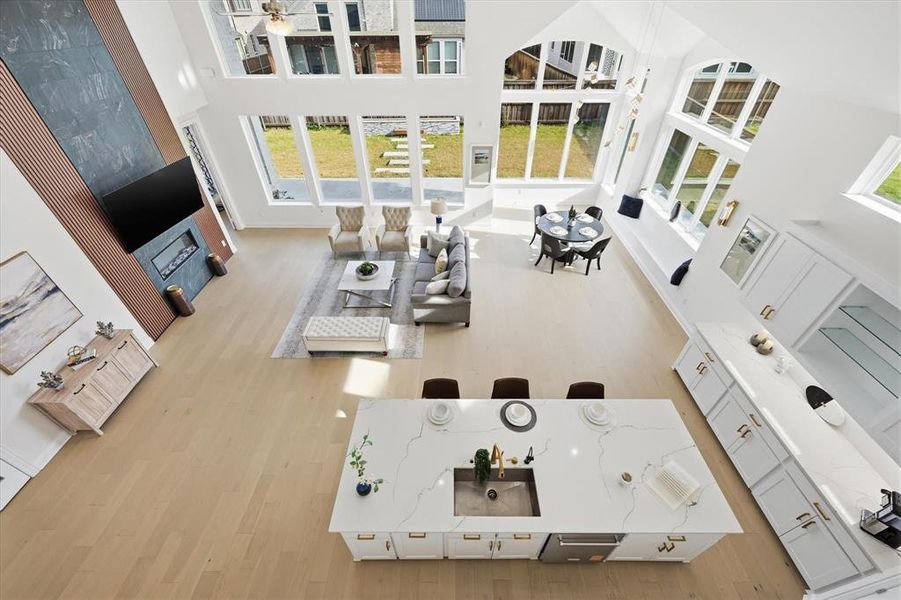 Expansive open-concept interior with vaulted ceilings, large arched and rectangular windows, light wood-finish flooring, a modern kitchen island with an undermount sink and white countertop, and a contemporary fireplace feature wall