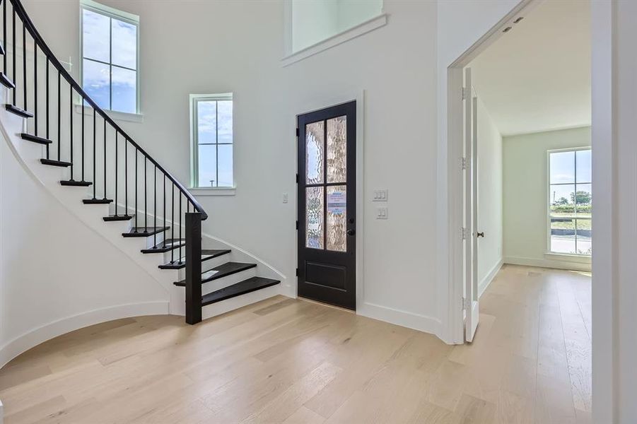 Foyer entrance featuring wood finished floors, stairs, baseboards, and a towering ceiling
