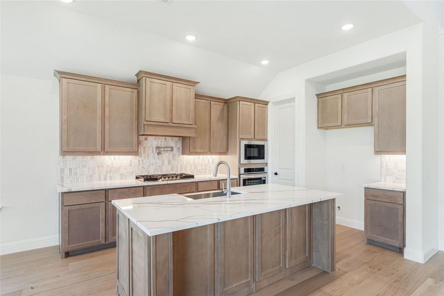 Kitchen with large center island, quartz countertops, wood cabinets, tile backsplash, and stainless steel appliances