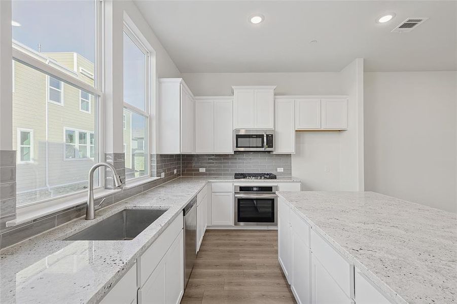 The kitchen features white cabinetry, light countertops, and stainless steel appliances, including a microwave, oven, and dishwasher