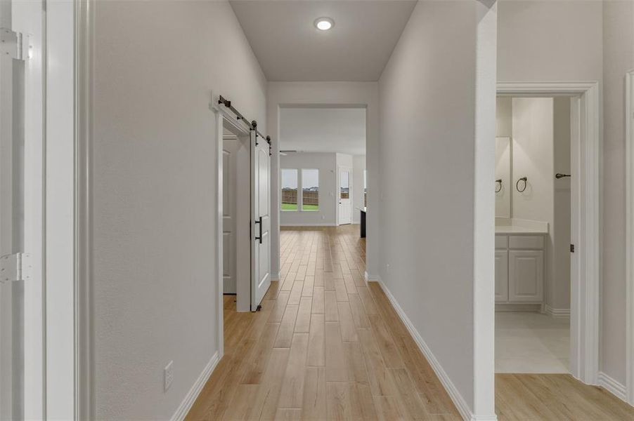 Hallway featuring wood-finish flooring, recessed lighting, and a modern barn door Hallway featuring wood-finish flooring, recessed lighting, and a modern barn door
