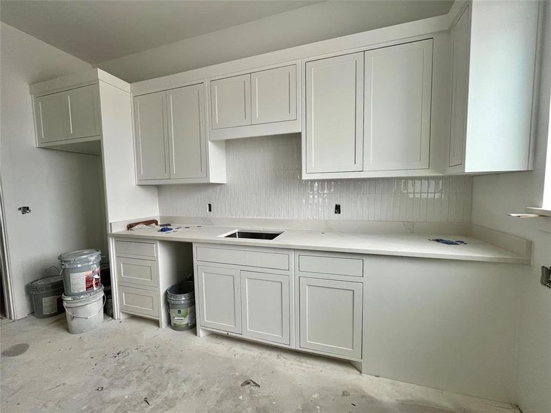 Kitchen featuring decorative backsplash, white cabinetry, and sink