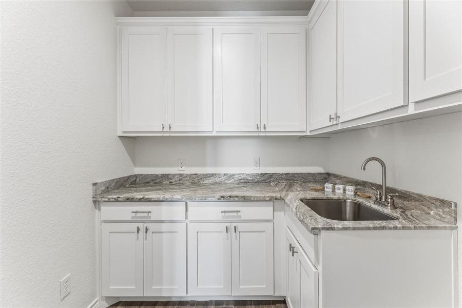 White cabinetry with stone counters and a utility sink create a functional laundry space.