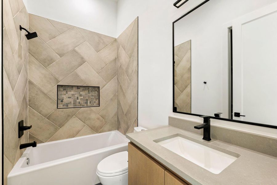 Bathroom featuring a white tub with matte black fixtures, herringbone-patterned wall tile with a mosaic-tiled niche, and a vanity with a light-toned countertop and wood-finish cabinetry