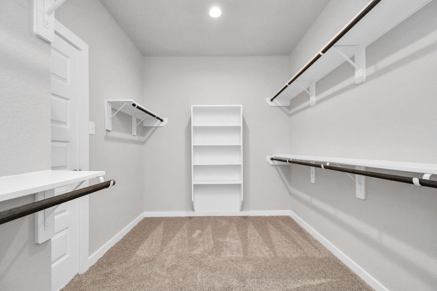 Expansive walk-in closet, adorned with high ceilings, luxurious carpet, and built in shelves. Sample photo of completed home with similar floor plan. Actual colors and selections may vary.