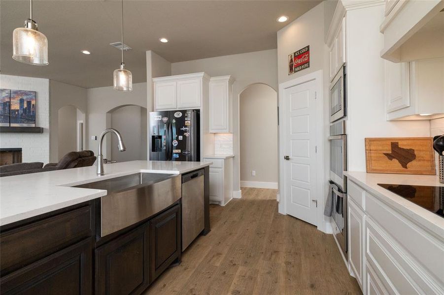 Kitchen featuring arched walkways, appliances with stainless steel finishes, light wood finished floors, white cabinetry, and recessed lighting