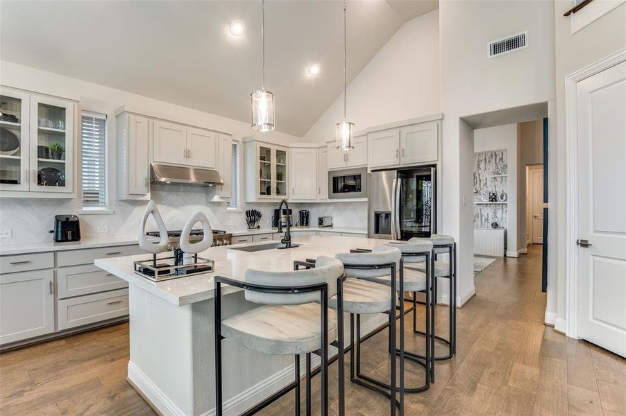 Kitchen featuring glass insert cabinets, a breakfast bar area, hanging light fixtures, backsplash, and high vaulted ceiling