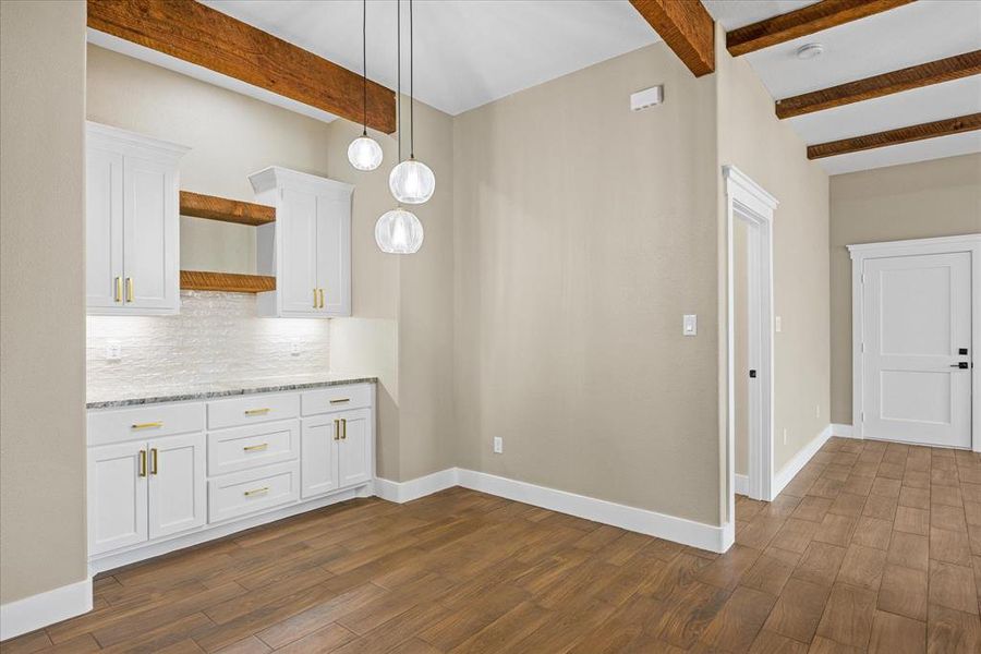 Kitchen featuring white cabinetry, backsplash, beam ceiling, dark wood finished floors, and light stone counters Kitchen featuring white cabinetry, backsplash, beam ceiling, dark wood finished floors, and light stone counters