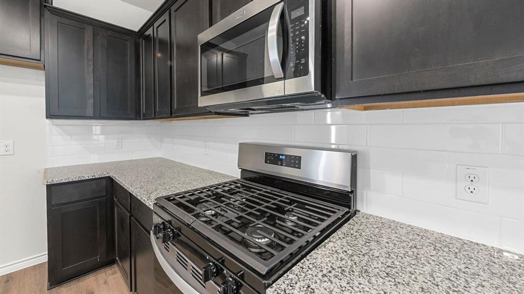 Kitchen with stainless steel appliances, light stone counters, backsplash, and dark cabinetry