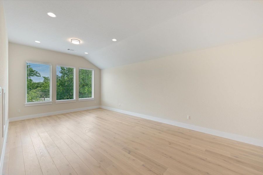 A naturally illuminated room features vaulted ceilings and light-toned hardwood flooring, creating an inviting blank canvas.