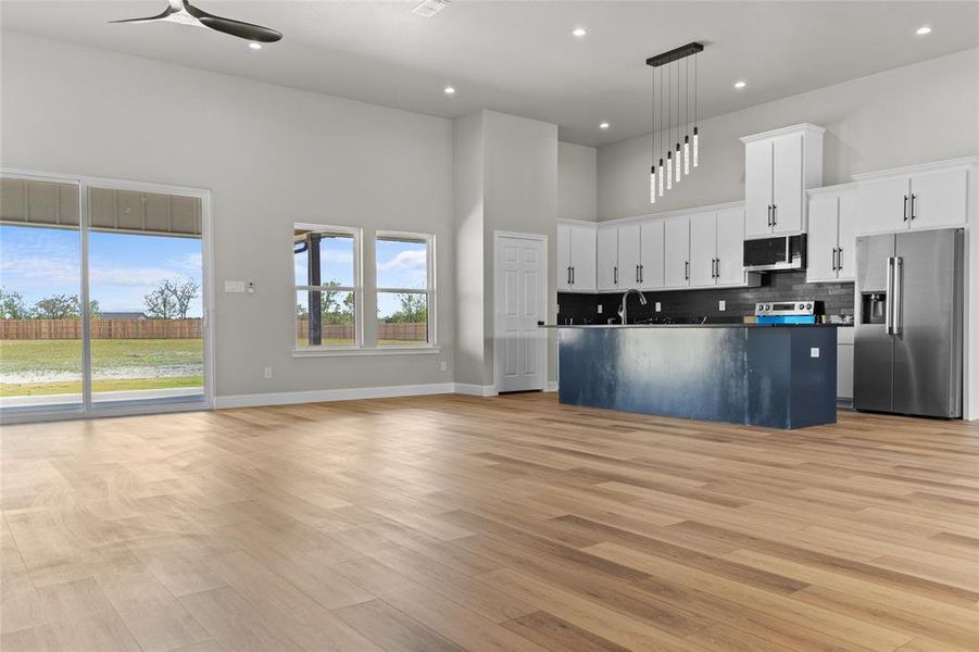 Kitchen with open floor plan, backsplash, stainless steel appliances, a high ceiling, and white cabinetry