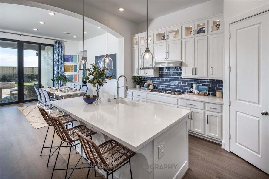 Kitchen featuring white cabinets, glass insert cabinets, decorative backsplash, dark wood-style flooring, and a breakfast bar area Kitchen featuring white cabinets, glass insert cabinets, decorative backsplash, dark wood-style flooring, and a breakfast bar area