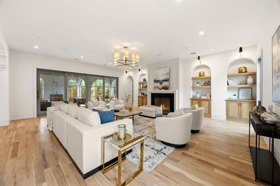 Spacious living area featuring wood-finish flooring, a fireplace with a light-toned mantel, built-in arched shelving with lower cabinetry, and a multi-pane sliding glass door Spacious living area featuring wood-finish flooring, a fireplace with a light-toned mantel, built-in arched shelving with lower cabinetry, and a multi-pane sliding glass door