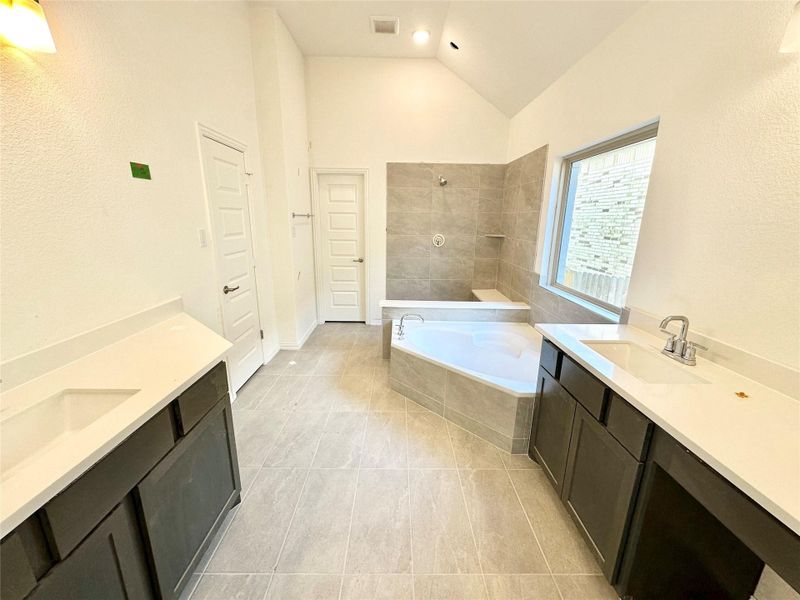 Full bath featuring two vanities, tiled bath, tiled shower, light tile patterned floors, and high vaulted ceiling Full bath featuring two vanities, tiled bath, tiled shower, light tile patterned floors, and high vaulted ceiling