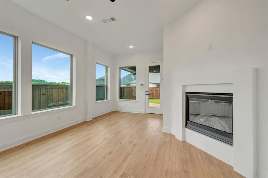 Living area with light wood-finish flooring, a contemporary fireplace, recessed lighting, and multiple large windows