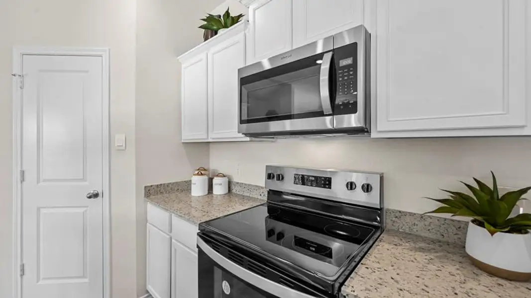 Kitchen with stainless steel appliances, white cabinetry, and light stone counters