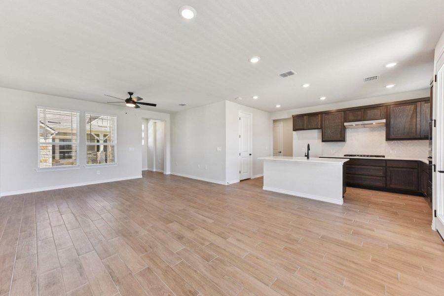 Kitchen with open floor plan, dark brown cabinets, recessed lighting, a center island with sink, and light wood finished floors