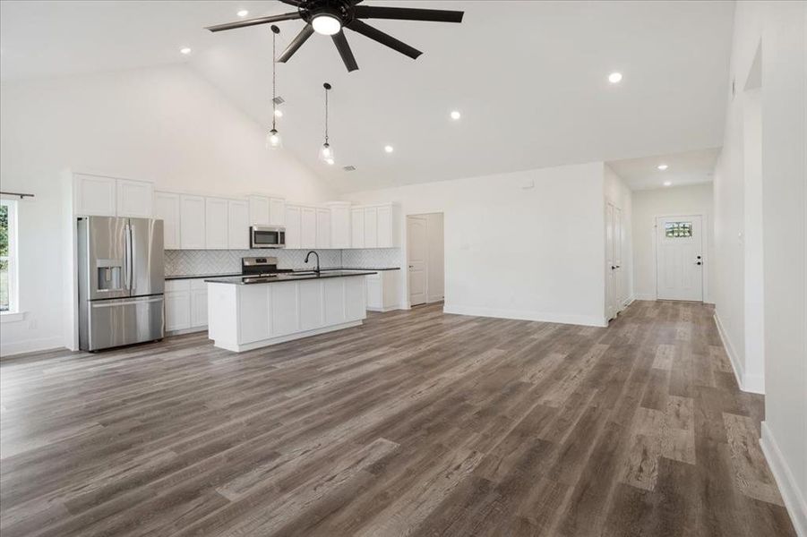 Kitchen with dark countertops, stainless steel appliances, open floor plan, white cabinets, and high vaulted ceiling