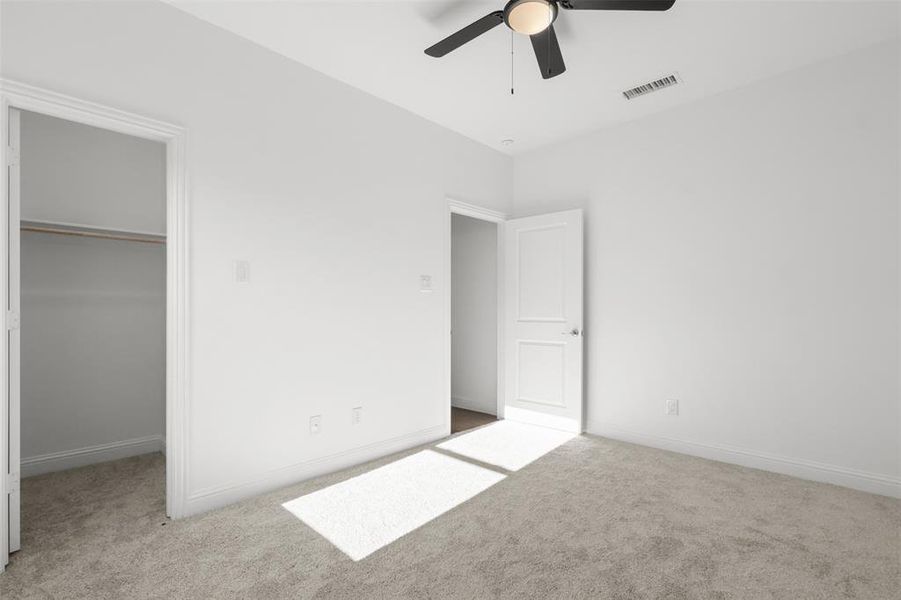 Unfurnished bedroom with ceiling fan, a walk in closet, light carpet, and a closet