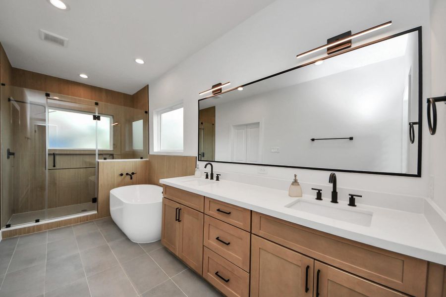 This stunning primary bathroom features a spacious layout with a sleek double vanity, luxurious soaking tub, and a modern glass-enclosed shower, offering a perfect blend of style and comfort.