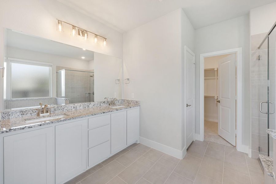 Master bathroom with double vanity, granite countertops, glass shower, and walk-in closet access Master bathroom with double vanity, granite countertops, glass shower, and walk-in closet access
