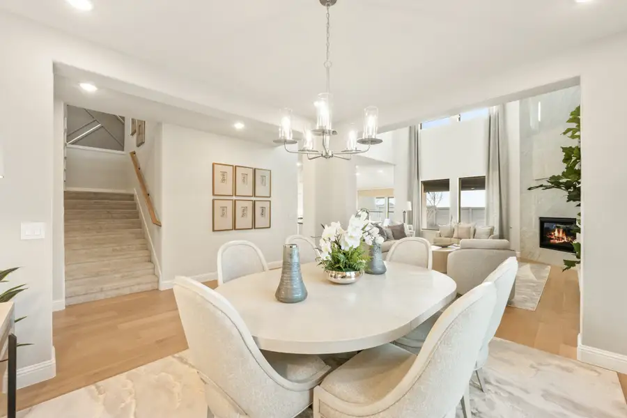 Dining room with oval white table, chandelier, and open view to living room with fireplace and staircase nearby