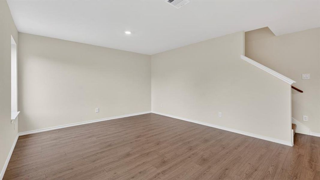 Spacious room featuring wood-finish flooring, light neutral wall tones, white baseboards, and a recessed ceiling light