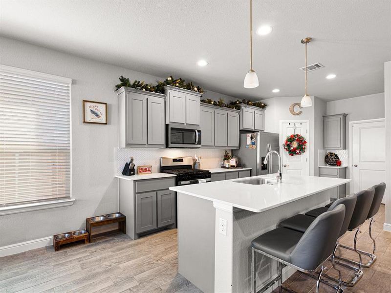 Kitchen with gray cabinetry, hanging light fixtures, and appliances with stainless steel finishes