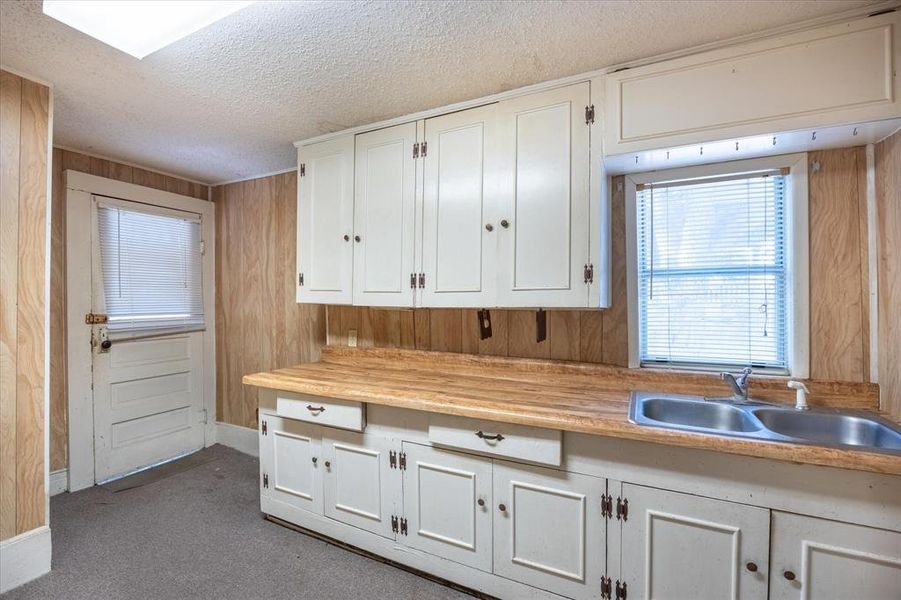 Kitchen with wood walls, a textured ceiling, white cabinets, and dark colored carpet