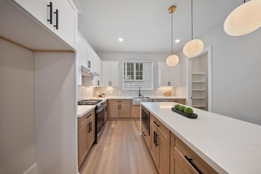 Modern kitchen featuring a spacious island with seating, elegant pendant lighting, and white cabinetry. Stainless steel appliances and a neutral color palette create a sleek, inviting atmosphere.