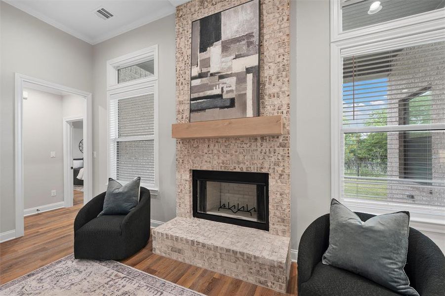Living area featuring visible vents, crown molding, a brick fireplace, wood finished floors, and baseboards