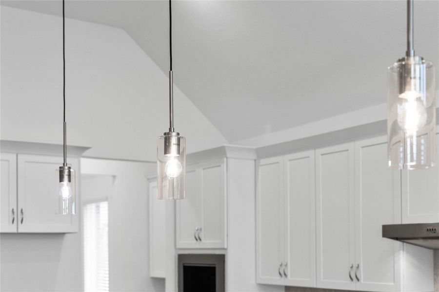 Three exquisite, clear glass pendant lights that elegantly hang above the kitchen island, providing focused task lighting and a touch of refined style.
