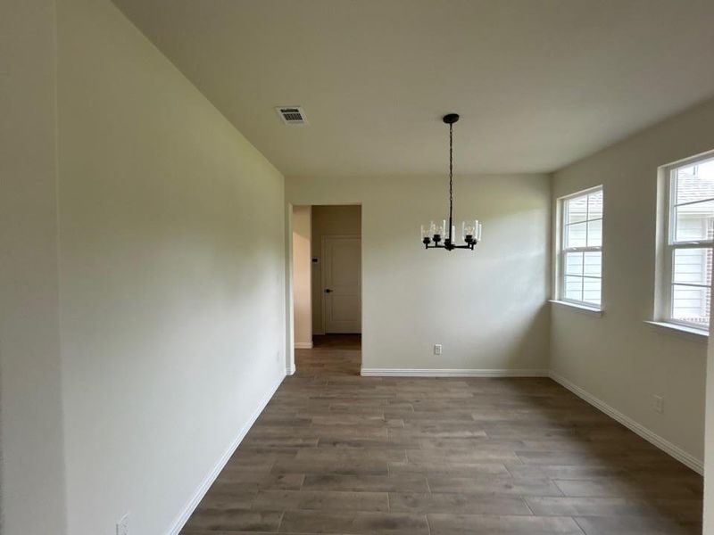 Spacious room featuring wood-finish flooring, a modern black chandelier, and multiple windows providing natural illumination