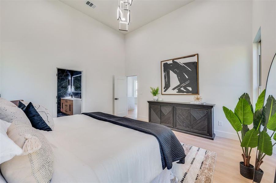 Bedroom featuring a towering ceiling, light hardwood / wood-style floors, and connected bathroom