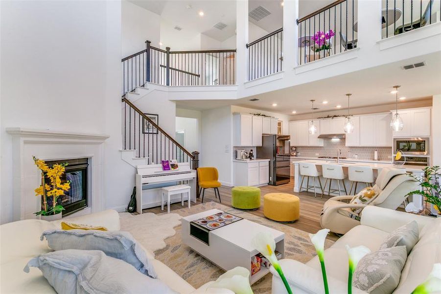 Living area with a high ceiling, light wood finished floors, stairs, recessed lighting, and a glass covered fireplace