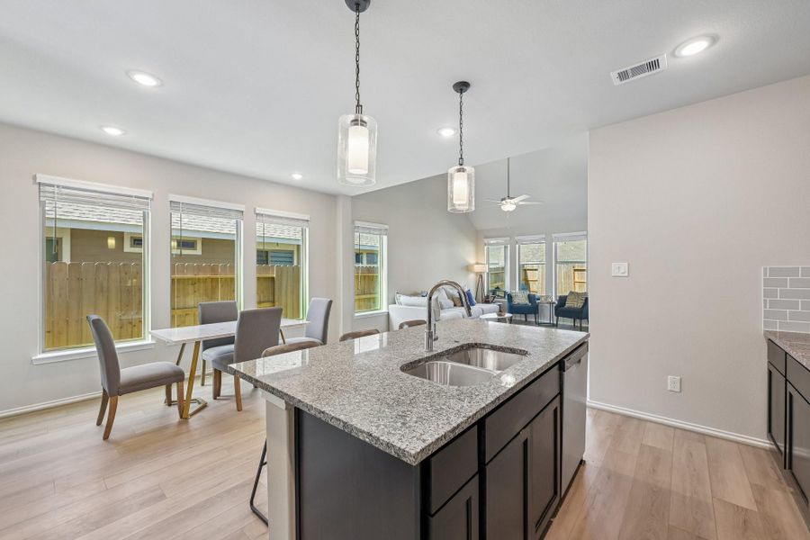 Bright and open kitchen with granite countertops and a spacious island flows seamlessly into a cozy living area, enhanced by large windows that offer abundant natural light.