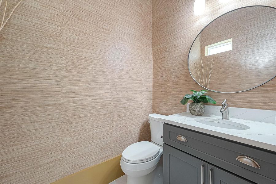 This is a modern bathroom with textured beige walls, a sleek gray vanity with white countertop, an oval mirror, and a small window providing natural light. This is a modern bathroom with textured beige walls, a sleek gray vanity with white countertop, an oval mirror, and a small window providing natural light.