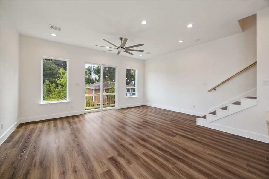 Bright, open living space filled with natural light from multiple oversized windows and a glass door leading to the outdoor area. Warm wood-look flooring adds contrast to the clean white walls, while recessed lighting and a dramatic modern ceiling fan enhance the airy atmosphere. The open layout offers excellent flexibility for living, dining, entertaining, and everyday relaxation. High ceilings and simple contemporary finishes make the room feel spacious, comfortable, and easy to personalize. Bright, open living space filled with natural light from multiple oversized windows and a glass door leading to the outdoor area. Warm wood-look flooring adds contrast to the clean white walls, while recessed lighting and a dramatic modern ceiling fan enhance the airy atmosphere. The open layout offers excellent flexibility for living, dining, entertaining, and everyday relaxation. High ceilings and simple contemporary finishes make the room feel spacious, comfortable, and easy to personalize.