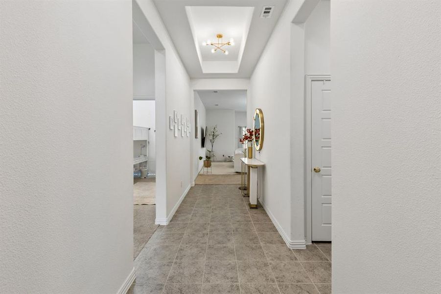 Tiled hallway featuring a tray ceiling with a modern light fixture, white baseboards, and textured walls
