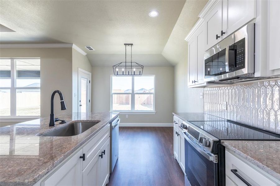 Modern kitchen featuring granite countertops, white cabinetry with matte black hardware, stainless steel appliances, and wood-finish flooring