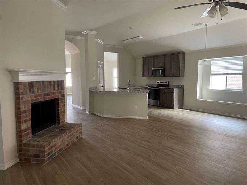 Kitchen featuring a fireplace, light stone counters, stainless steel appliances, light hardwood / wood-style floors, and ceiling fan